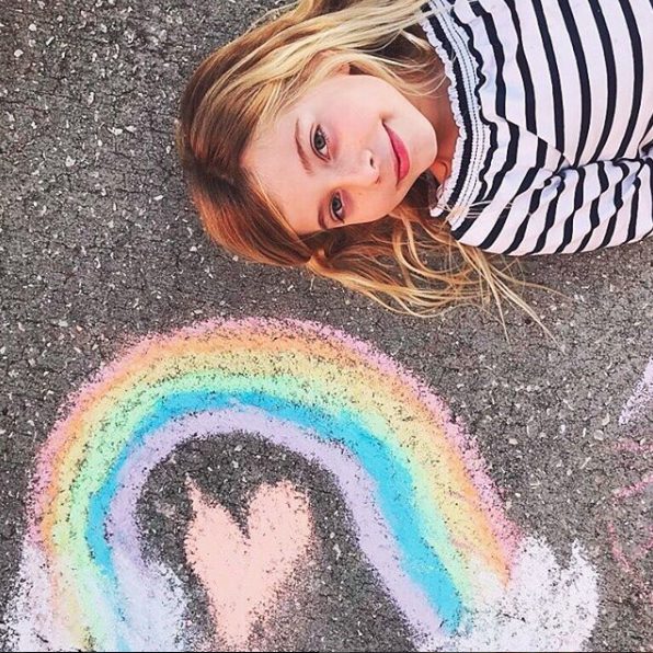 Child in striped shirt lying next to colorful chalk rainbow drawing on pavement