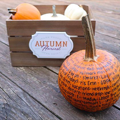 Decorative autumn display with a wooden crate containing orange and white pumpkins labeled "Autumn Harvest," and a textured orange pumpkin with handwritten memories in the foreground.