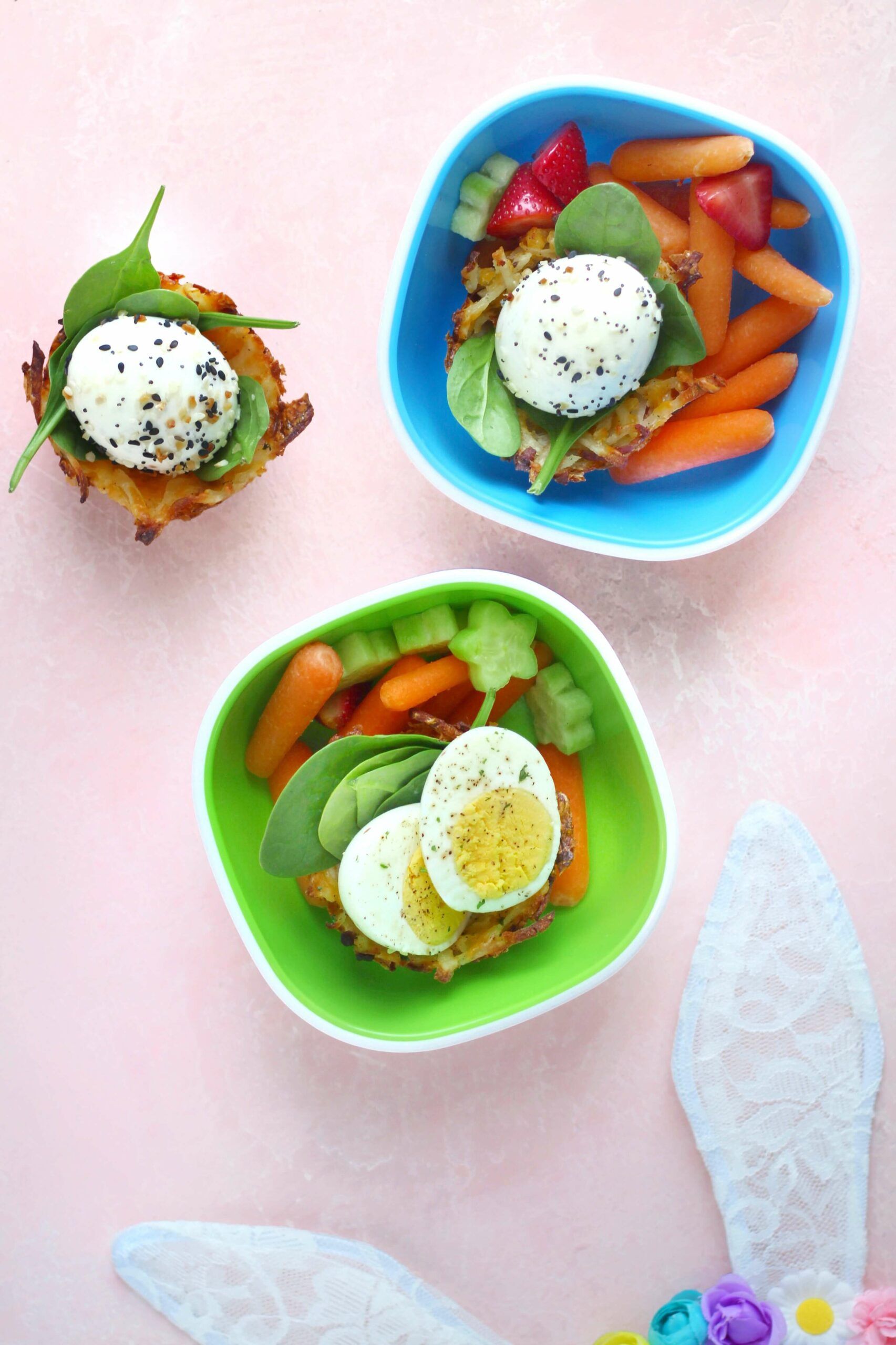 Healthy toddler meals in bright blue and green bowls featuring hash brown patties topped with soft cheese, fresh vegetables, and hard-boiled eggs, served with colorful finger foods and decorative fairy wings.