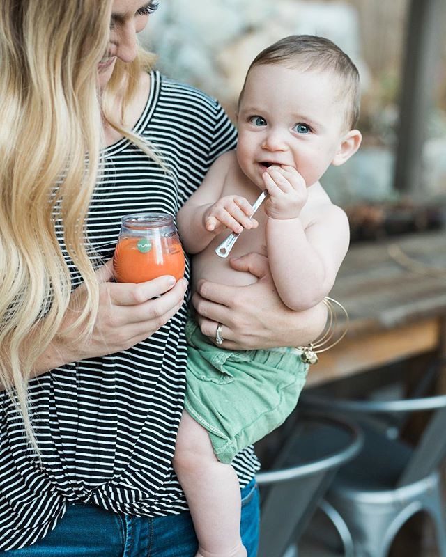Mother holding toddler who is drinking from a Munchkin sippy cup with orange juice inside.