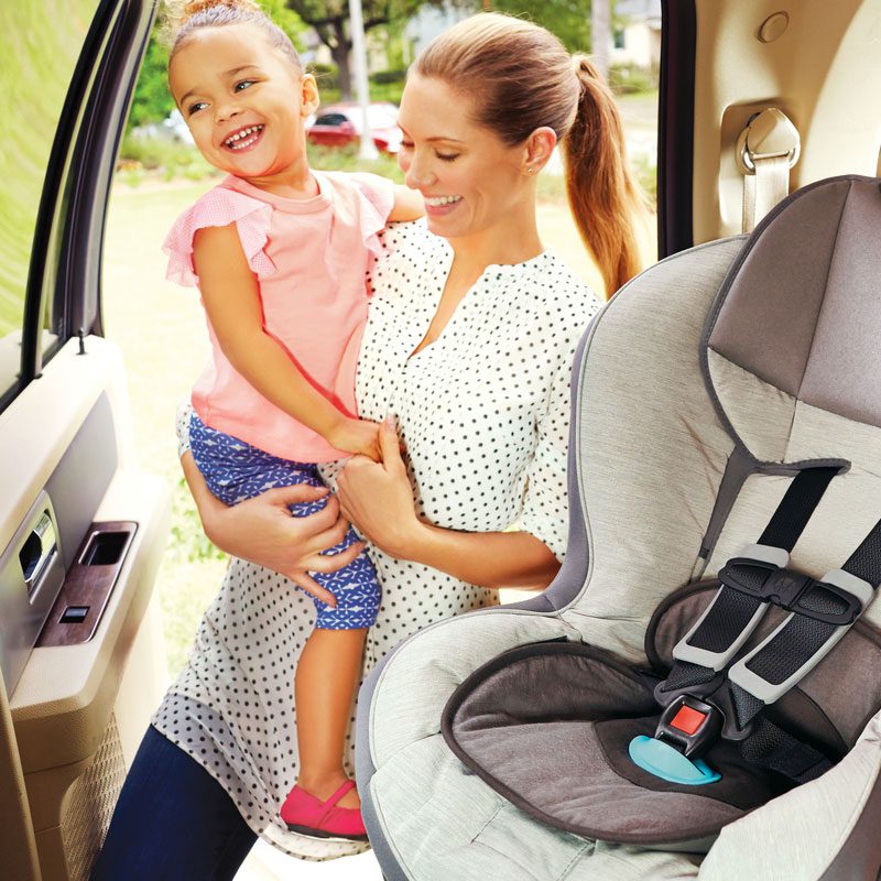 Mother holding toddler in car doorway next to gray and black Munchkin car seat installed in back seat.