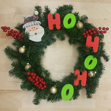 Christmas wreath with green garland, red and green "HO HO HO" letters, Santa face decoration, red berries, and gold ornaments.
