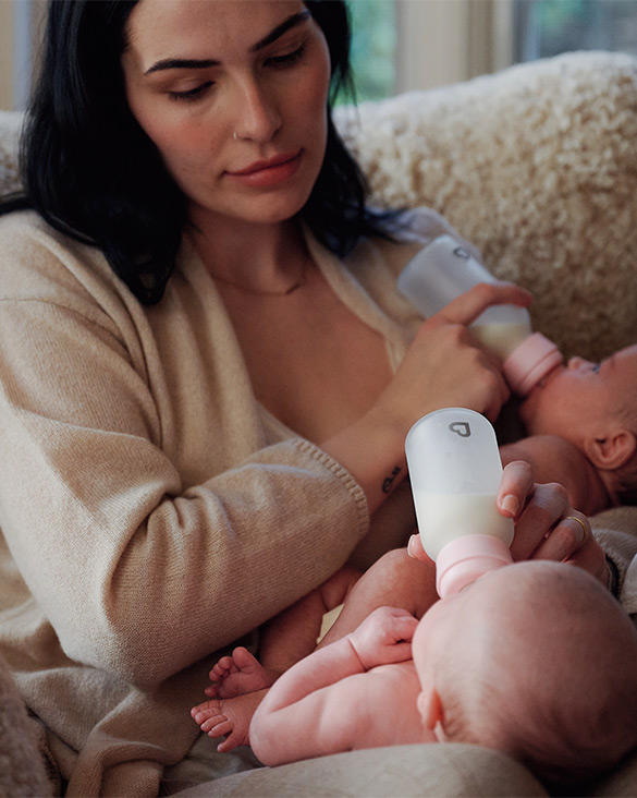 Woman feeding a newborn with a Munchkin bottle on a couch.