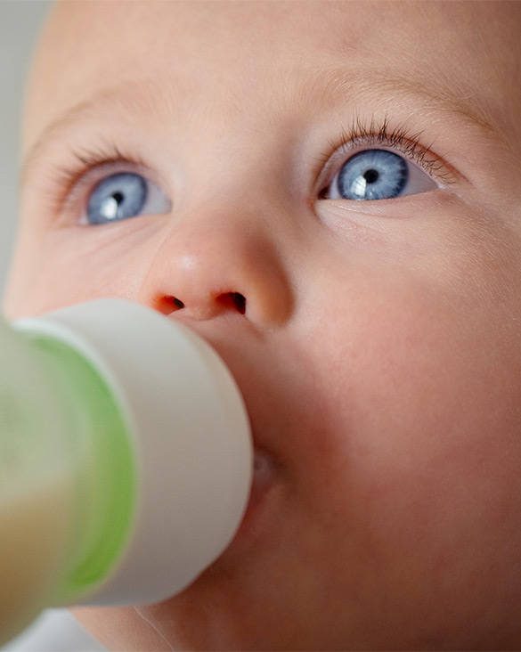 Baby with blue eyes drinking from a green and white sippy cup.