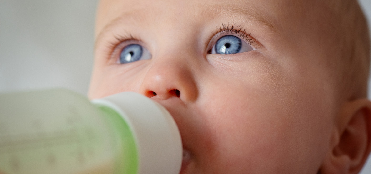 Baby with blue eyes drinking from a sippy cup with green and white coloring.