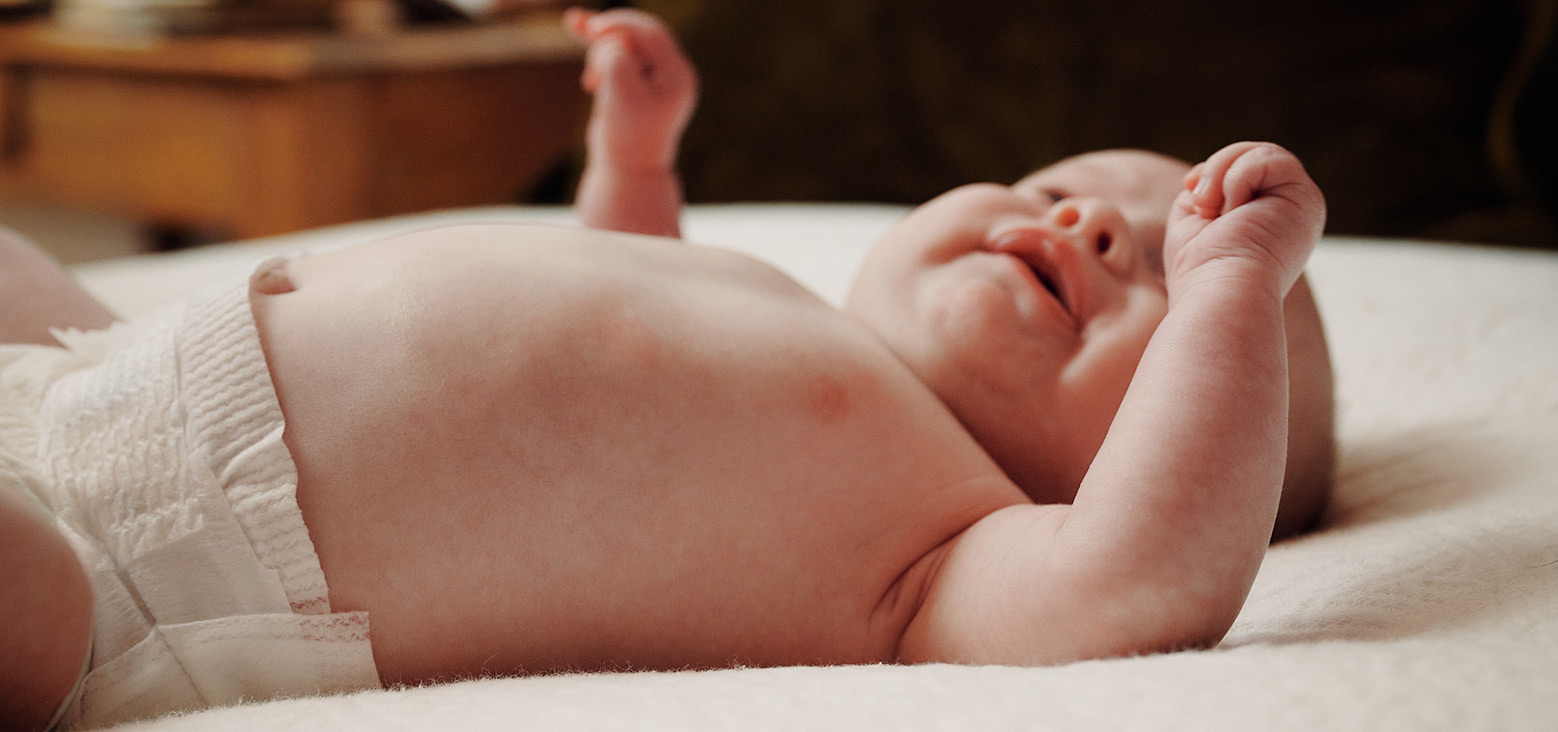Newborn baby lying on white bedding with arms and legs raised