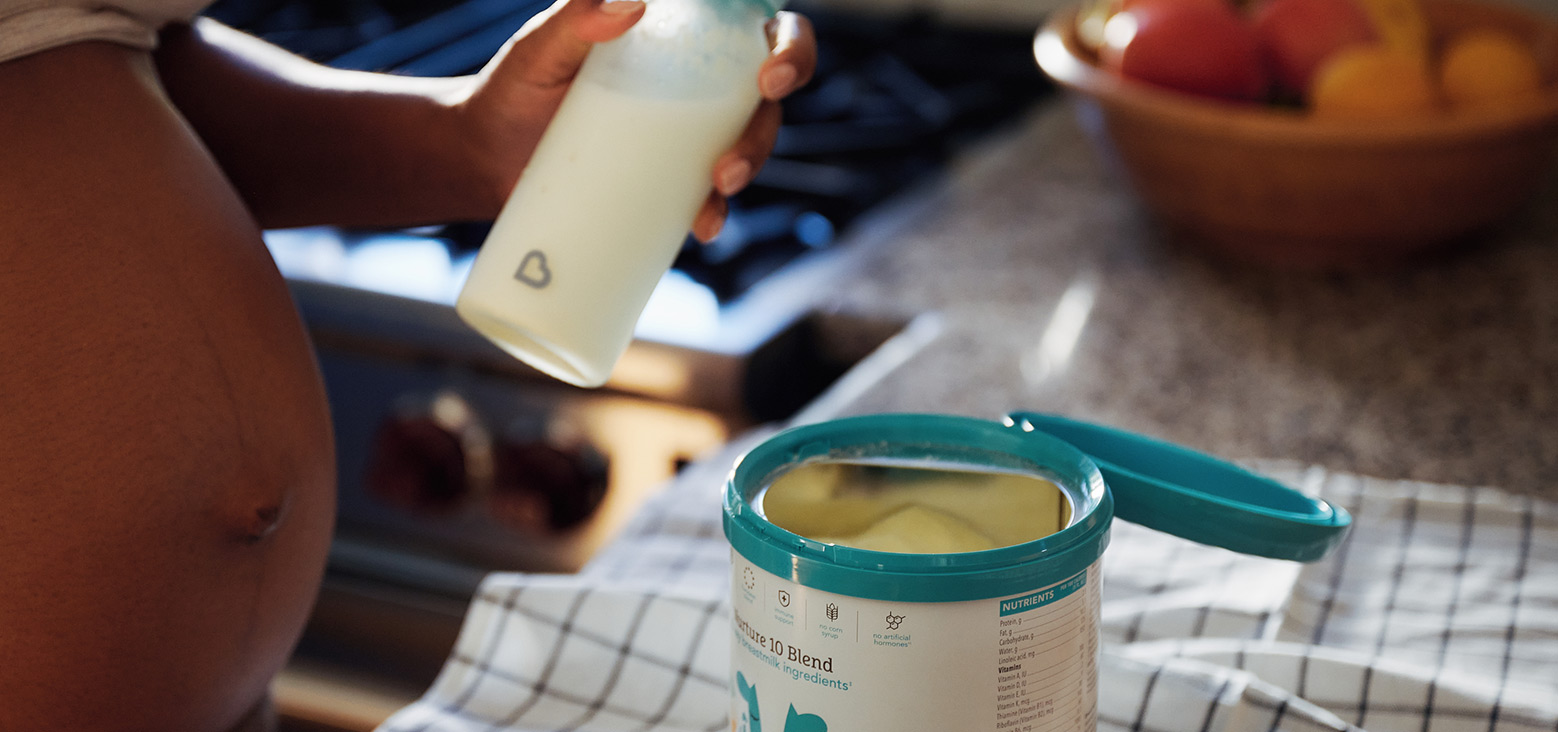 Toddler holding a Munchkin cup while sitting at a table with a container of infant formula and a scoop nearby.