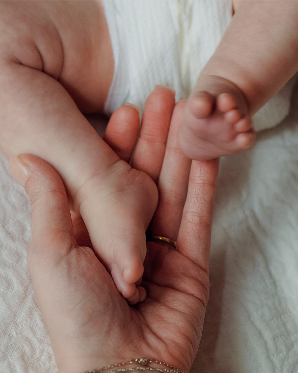 Newborn baby's hand grasping adult's finger, wrapped in white cloth.