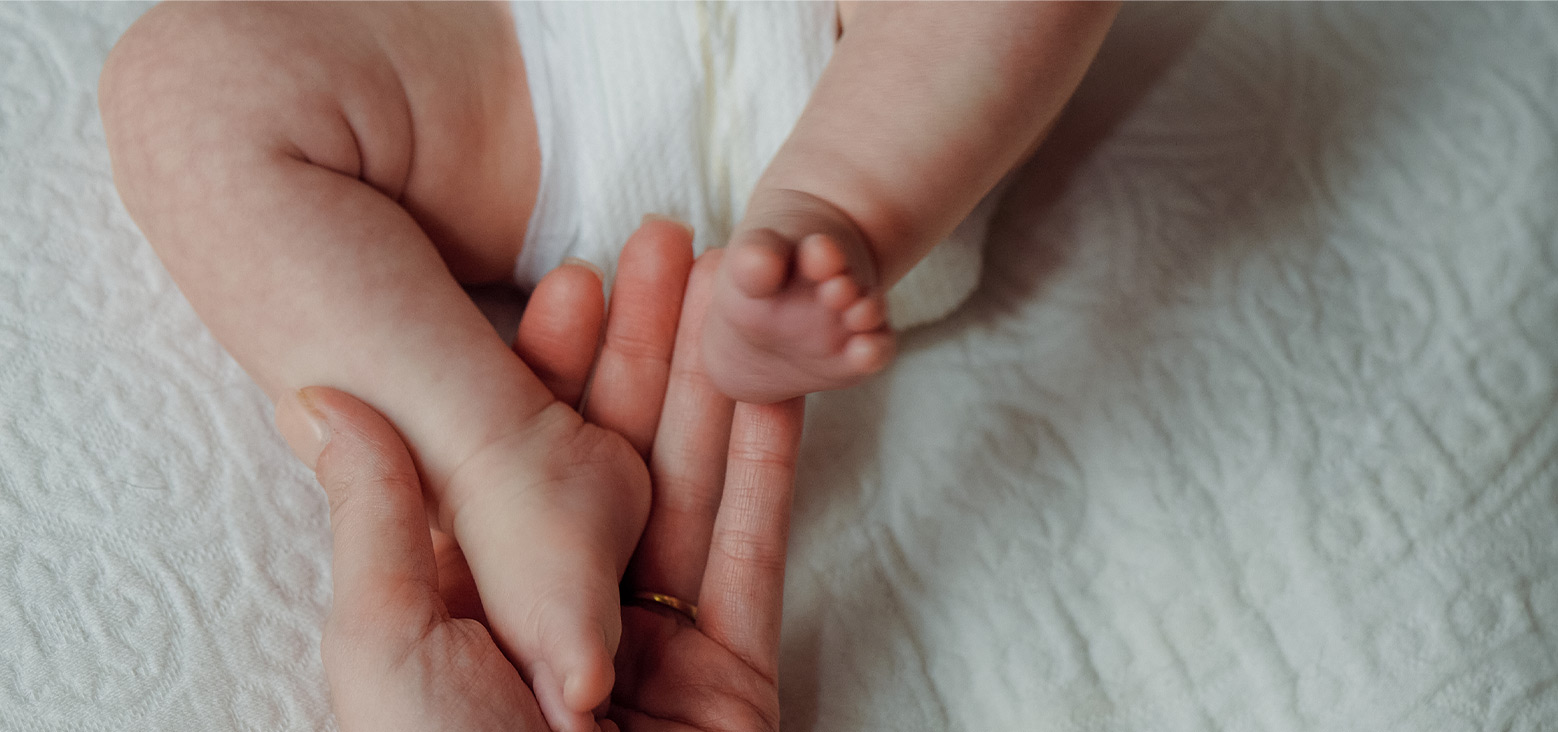 Baby's tiny feet resting in an adult's hands on a white textured blanket.