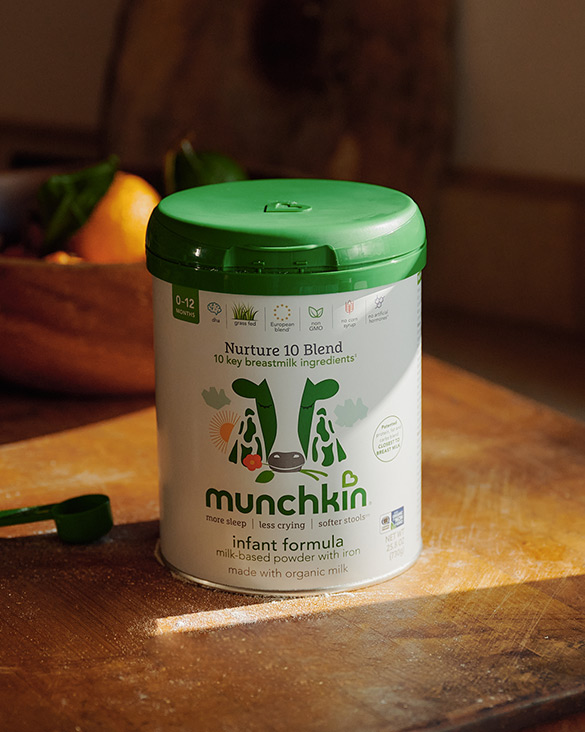 Munchkin Nurture 10 Blend infant formula container with green lid on a wooden surface, surrounded by fresh produce.