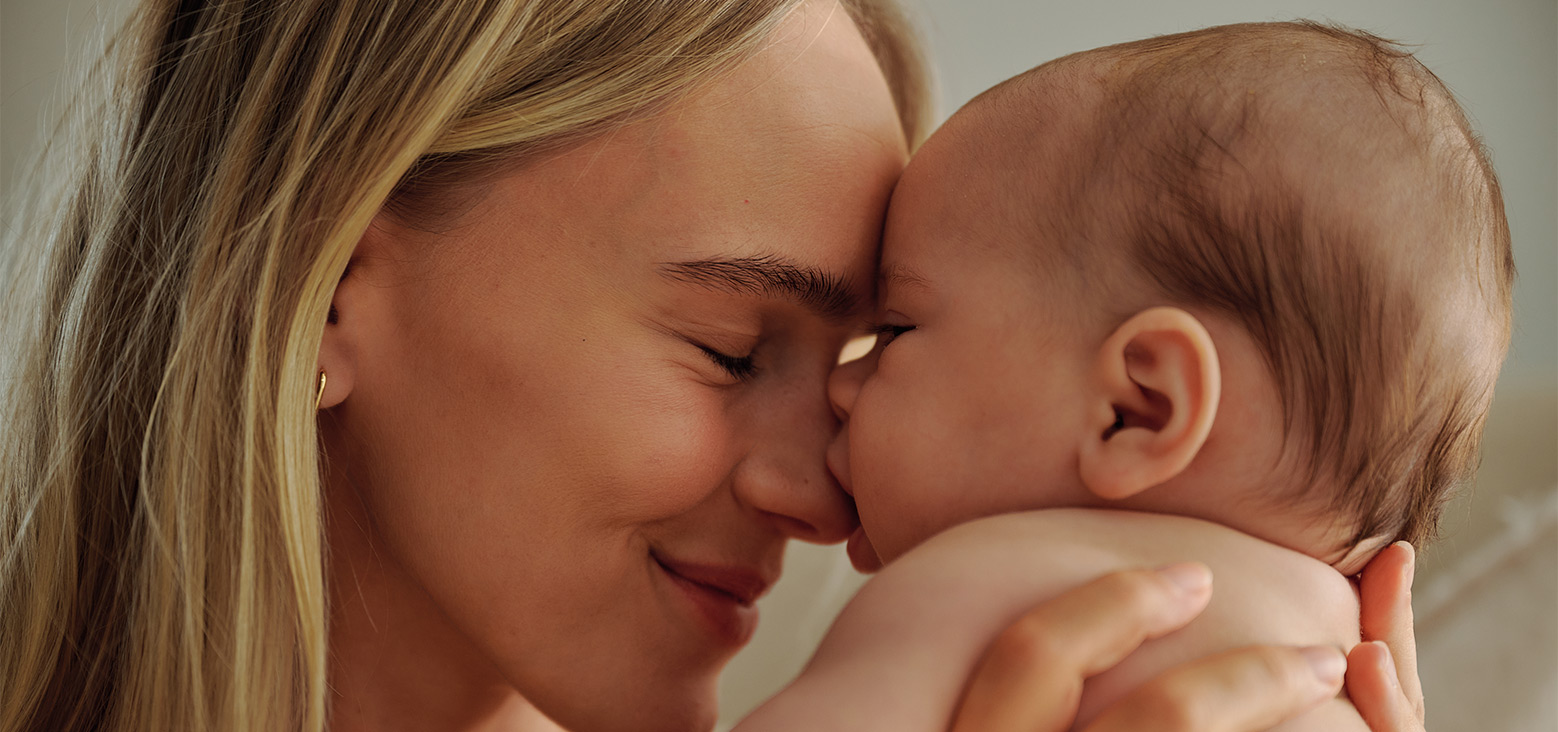Mother with blonde hair kissing her infant baby, tender parenting moment