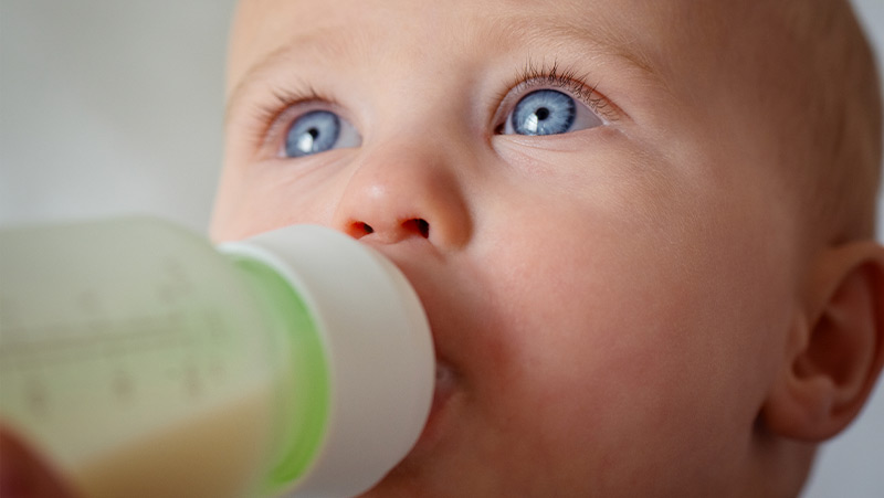 Baby with blue eyes drinking from a sippy cup with green accents.