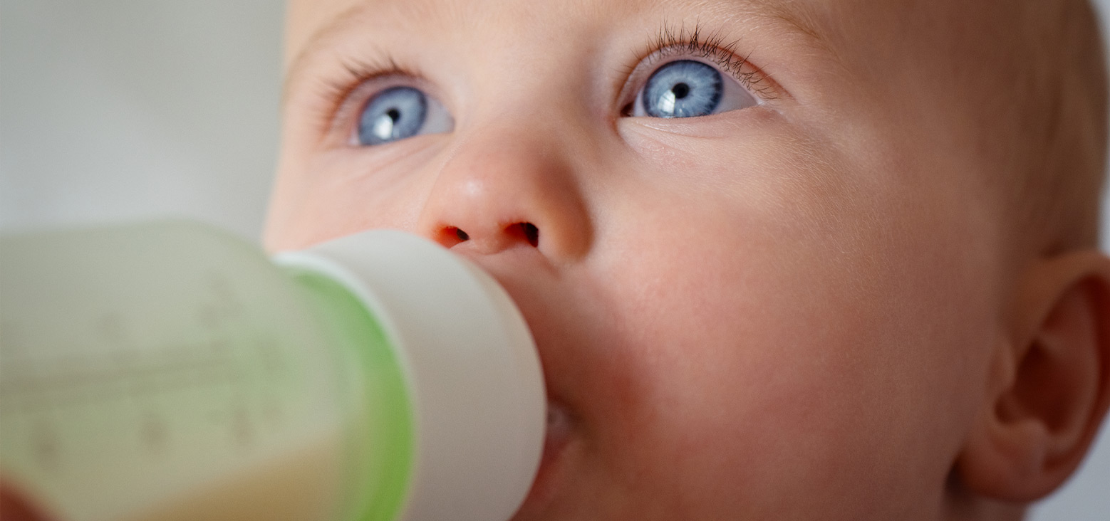 Baby with blue eyes drinking from a green and white cup.