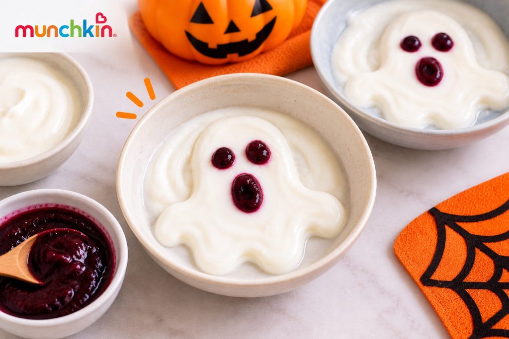 Halloween yogurt ghost bowls made with plain yoghurt shaped into ghosts and decorated with smooth berry purée eyes and mouths, served in shallow bowls with festive pumpkin decorations.